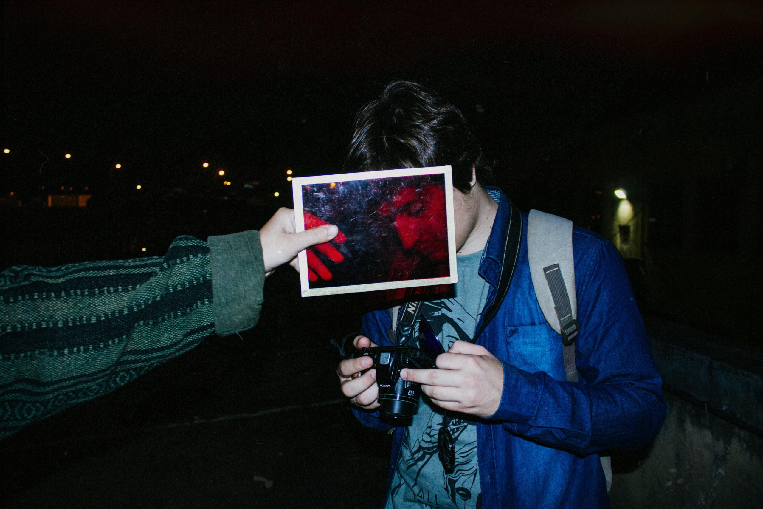 Unique night photography featuring a person holding a camera with a red overlay reflecting their face.