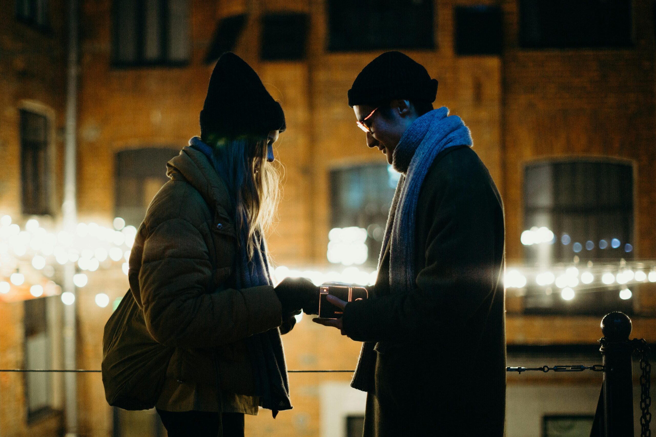 A couple enjoys a romantic moment with a gift, set against urban lights in the evening.